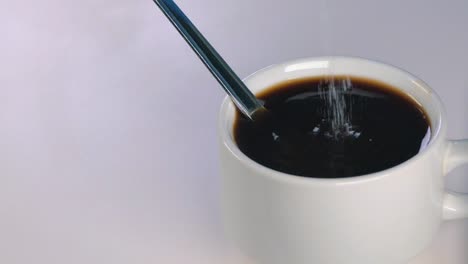 slow motion shot of white sugar being poured into a black coffee