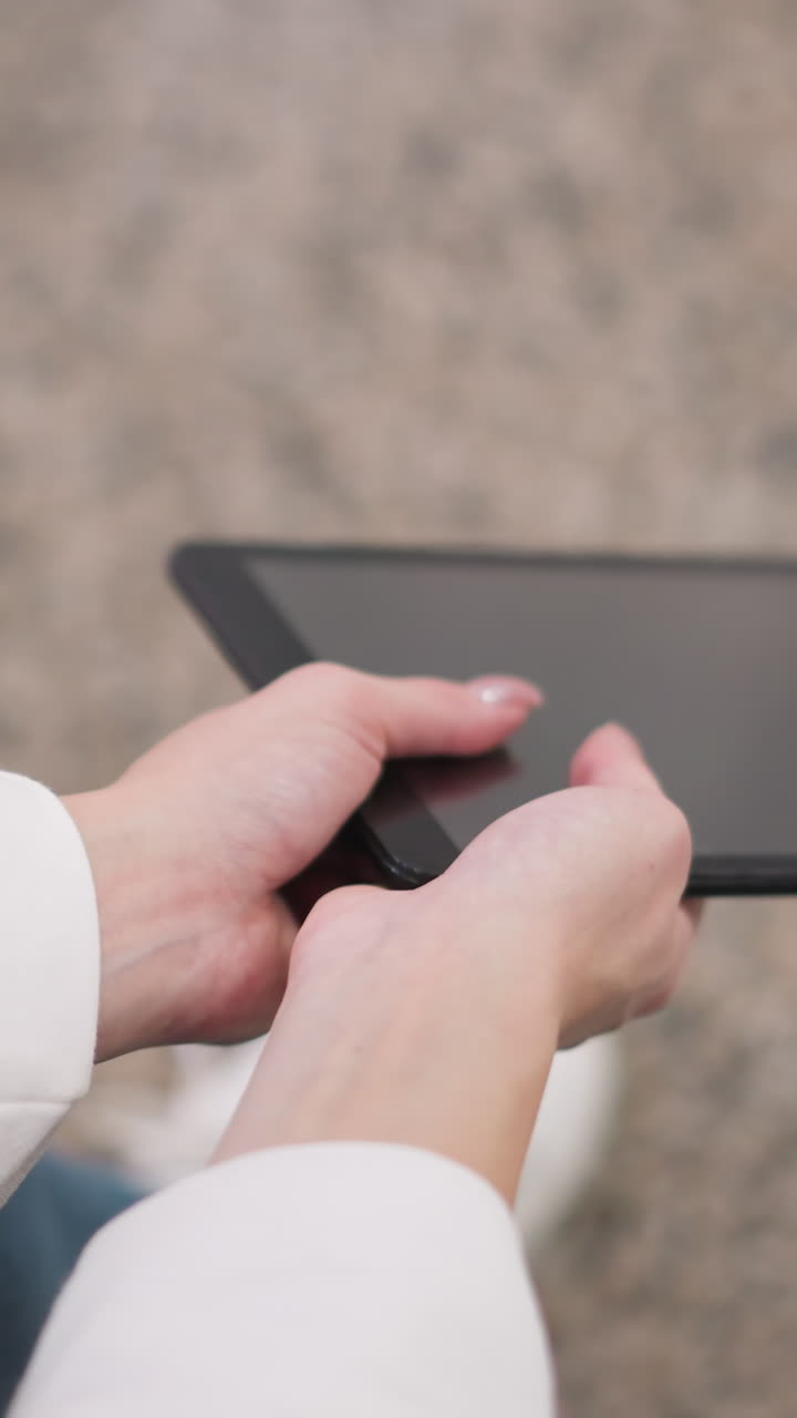 cerca de las manos en la manga blanca sosteniendo suavemente la tableta mientras está sentado en el suelo de granito, las manos balancean la tableta ligeramente, creando reflejos sutiles en la pantalla