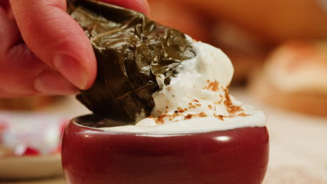 Hand Dipping Stuffed Grape Leaves in Yogurt Sauce