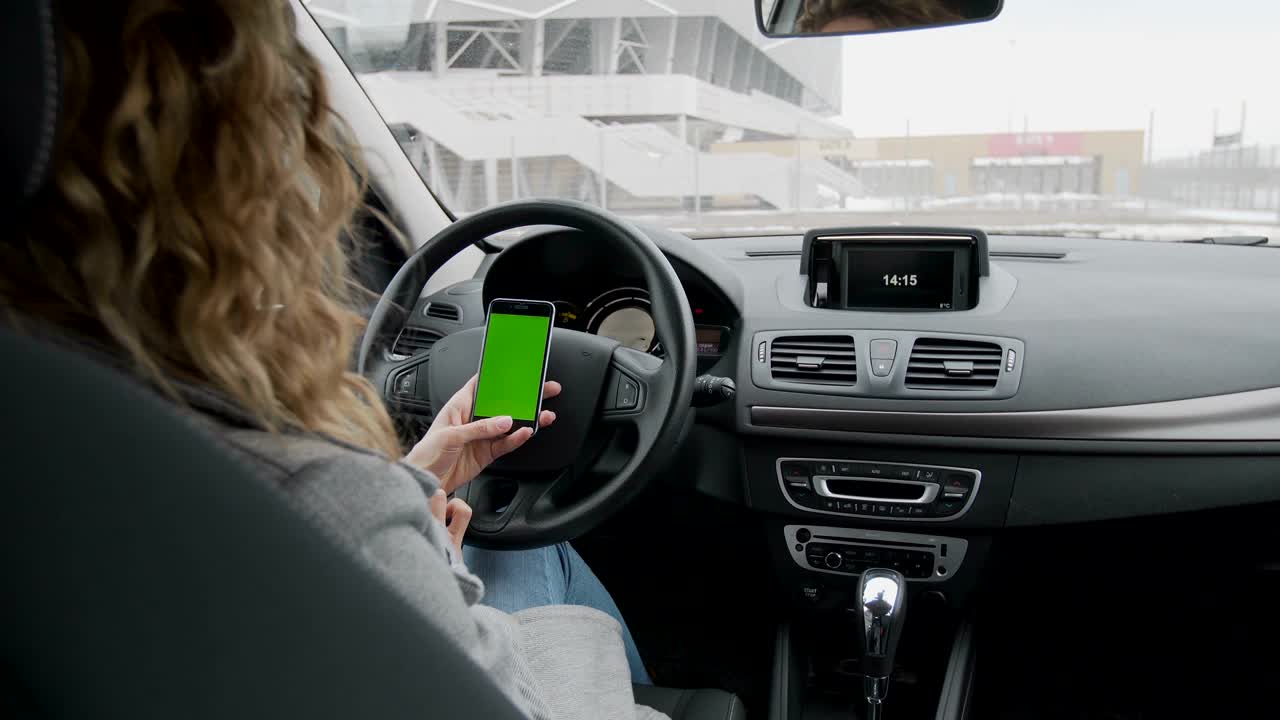 mujer se sienta en el coche moderno y trabaja en el teléfono inteligente - manos de primer plano. pantalla verde. llave croma