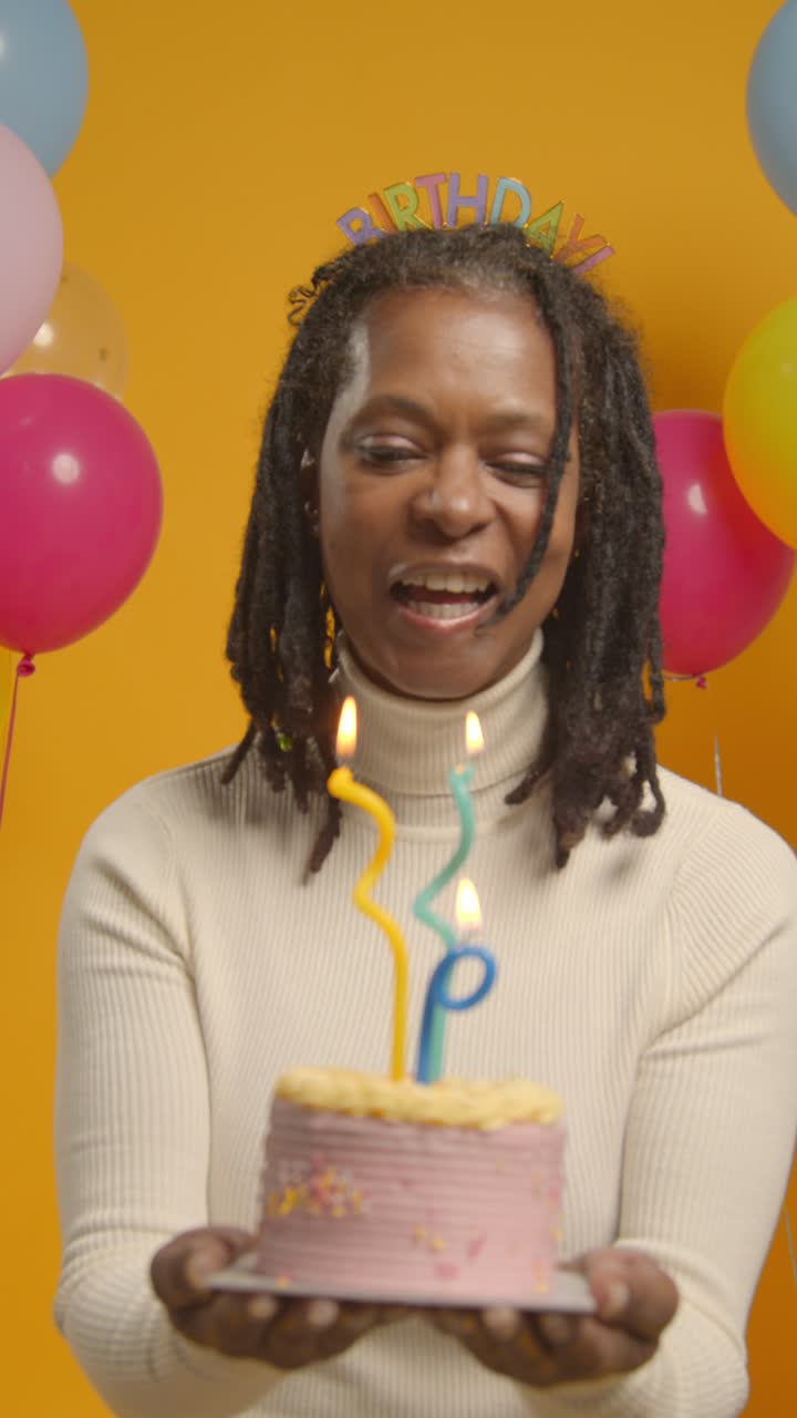 retrato vertical de estudio de video de una mujer con una cinta para la cabeza de cumpleaños celebrando su cumpleaños soplando velas en el pastel