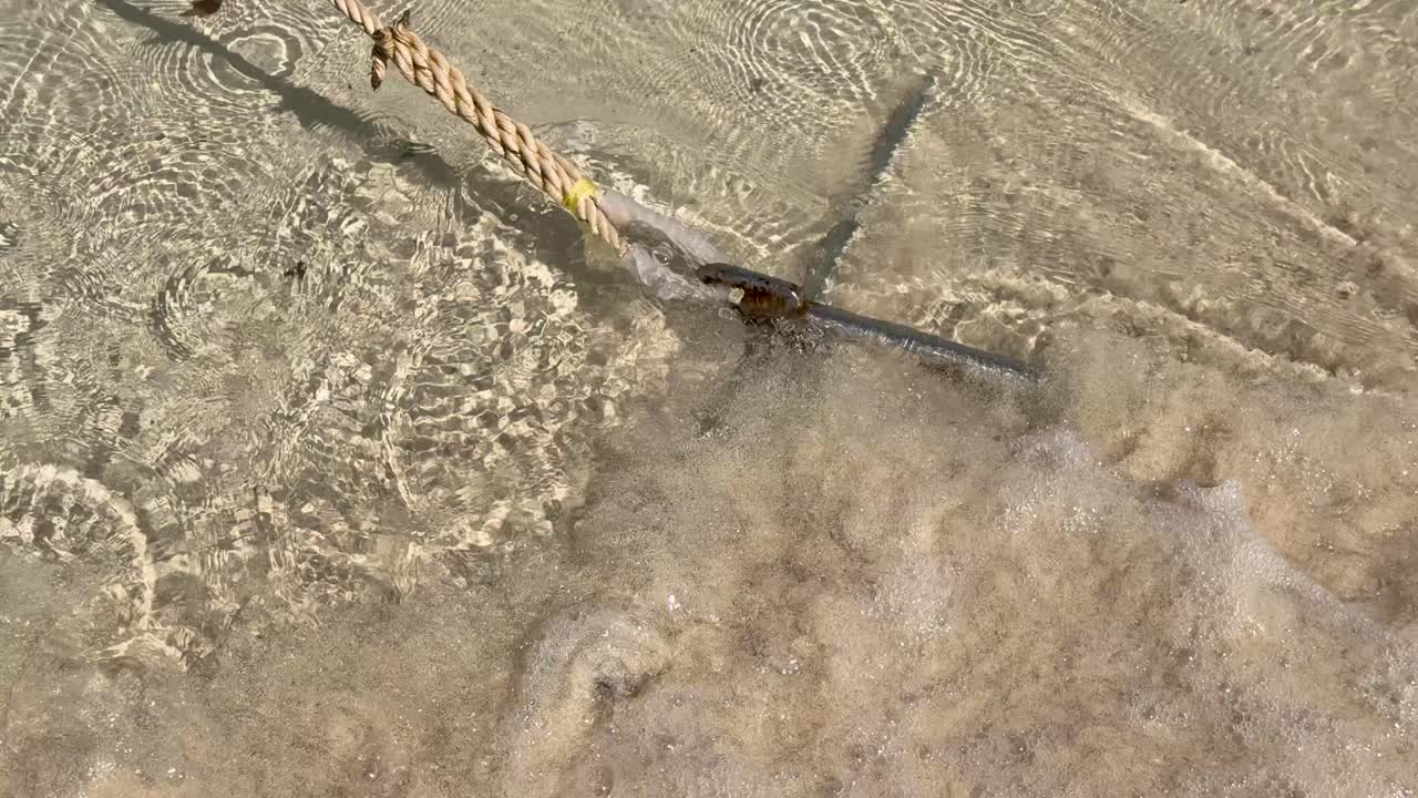 Primo piano di un'ancora di metallo e una corda sulla sabbia mentre le onde dell'oceano si infrangono