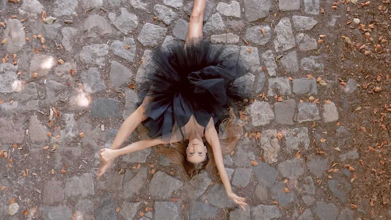 bailarina de ballet caucásica rubia con tutu negro moviéndose en el suelo