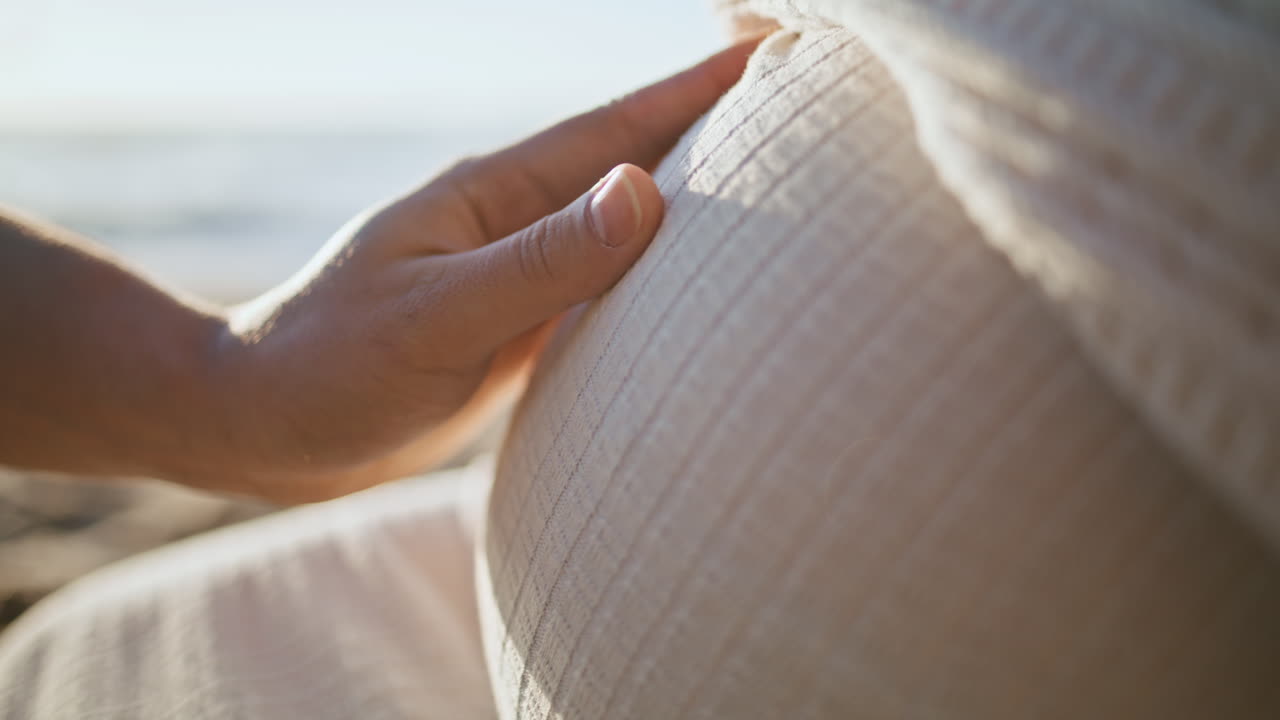 미래의 아버지 손이 임신한 배를 만지는 아내 해변에 앉아 해가 지는 가까운