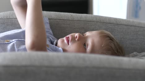 Young-boy-laying-on-couch-and-talking,-indoors-static-view
