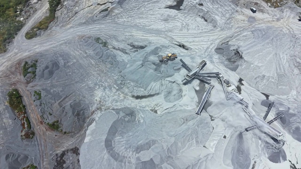 Operations at a granite quarry showing machinery and piles of stone in a large, active work site near a rural area during daylight hours