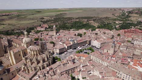 aerial view over plaza mayor beside segovia cathedral on sunny day with rural fields in distant background