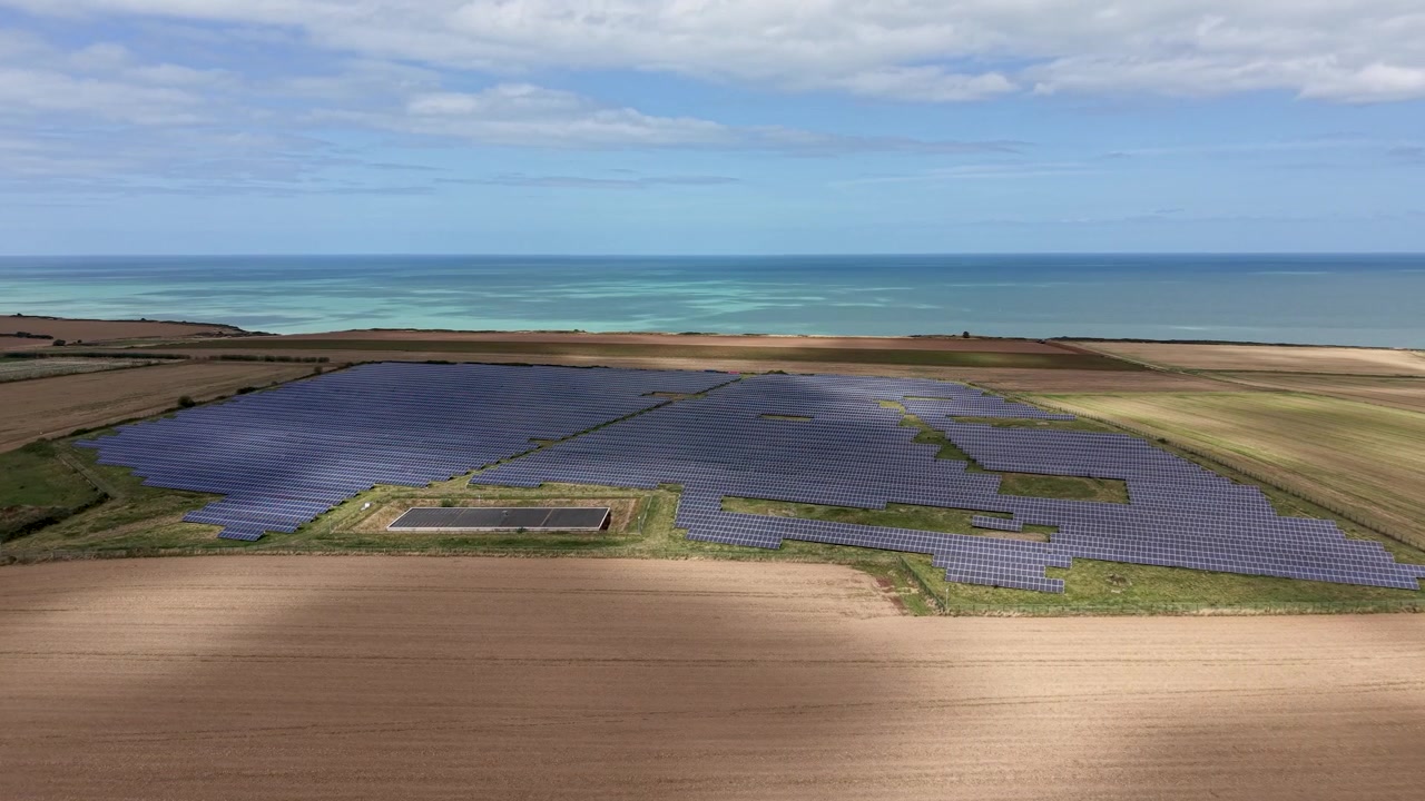 Riprese di un grande parco solare attraverso campi agricoli lungo la costa della Normandia in Francia, con il mare e la costa visibili sullo sfondo