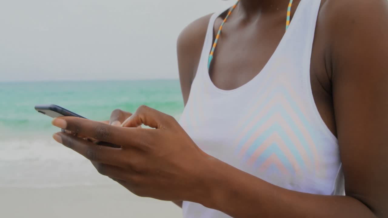 vista frontal de una mujer afroamericana usando teléfono móvil en la playa 4k
