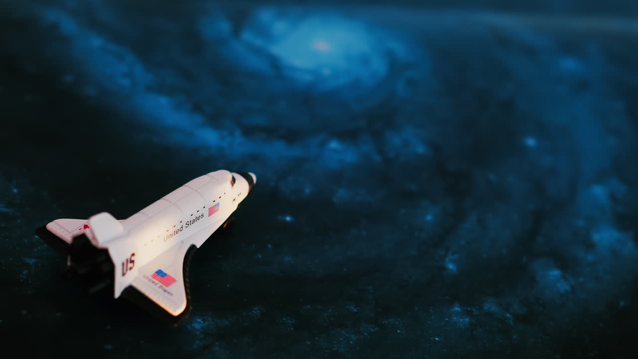Close up of a miniature toy space shuttle placed on a blue cosmic galaxy backdrop