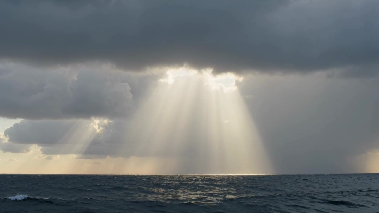 Fasci di luce solare centrali che emergono da una stretta fessura tra le nuvole fino all'oceano, proiettando una fascia d'acqua luminosa.