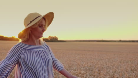 a young woman in a hat looks at the sunset over the wheat field