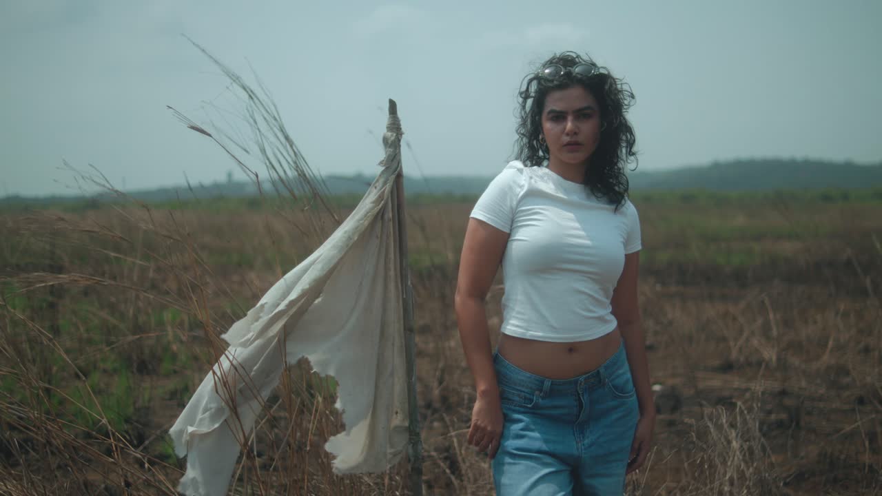 Woman stands in dry field under blue sky, feeling contemplative and calm