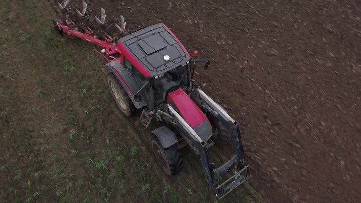 Ripresa aerea ravvicinata in tracking di un trattore che ara il campo di un agricoltore