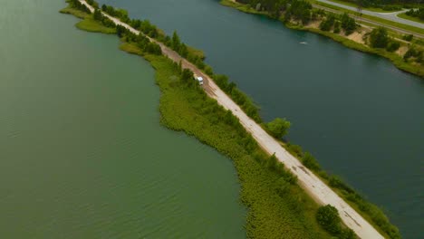 Aerial drone footage flying over a mining road made in between teo large artificial lakes where a truck is driving from a open pit sand quarry mine during a cloudy day with a highway visible, Männiku
