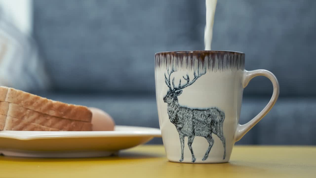 vertiendo leche caliente en la taza de cerámica con diseño de renos al lado del plato de pan cortado