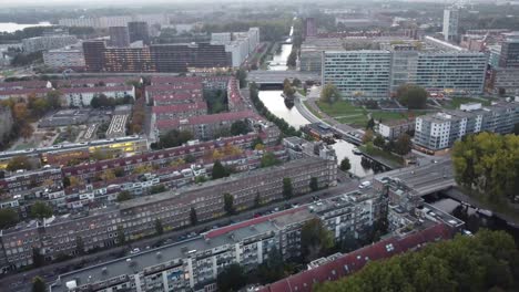 You-can-see-one-of-the-many-canals-in-the-historic-Amsterdam-and-its-suburbs,-with-buildings-parallel-to-each-other-and-areas-of-lush-trees-in-the-sunset,-splendid-aerial-view