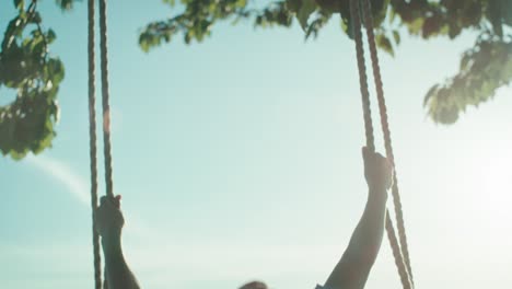 little girl swinging high in summer day during the golden hour.