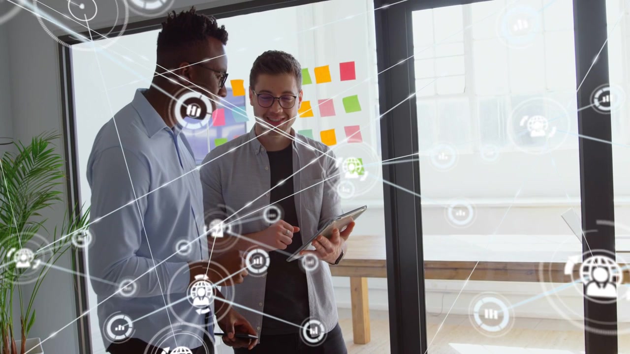 Two male colleagues tapping tablet in office, generating network overlay while reviewing product