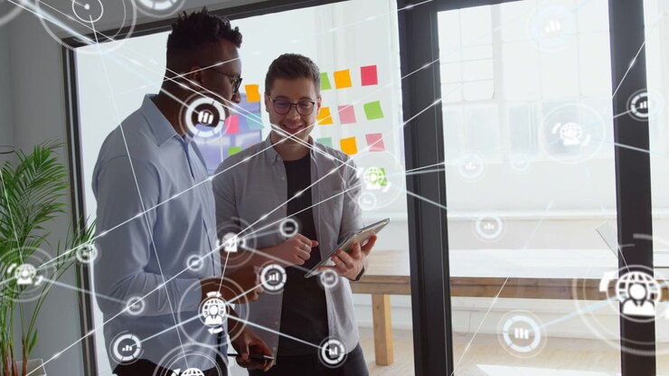 Two male colleagues tapping tablet in office, generating network overlay while reviewing product