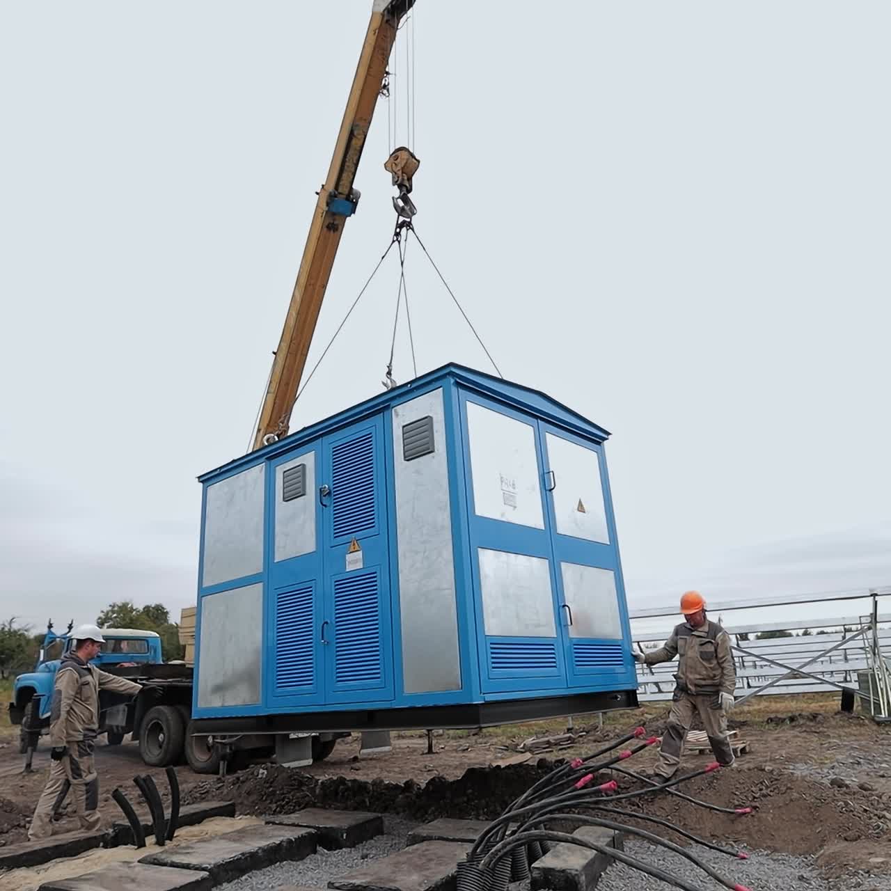 Metal booth being lifted up with the help of crane. Workers controlling the process and heading equipment to necessary site