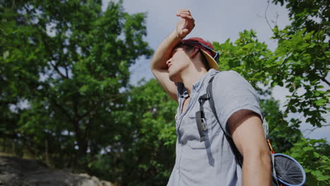 man-looking-into-the-sun,-sunny-athletic-young-guy,-snapback-hat,-summer-vibes,-hiking-in-the-forest,-trail-walking