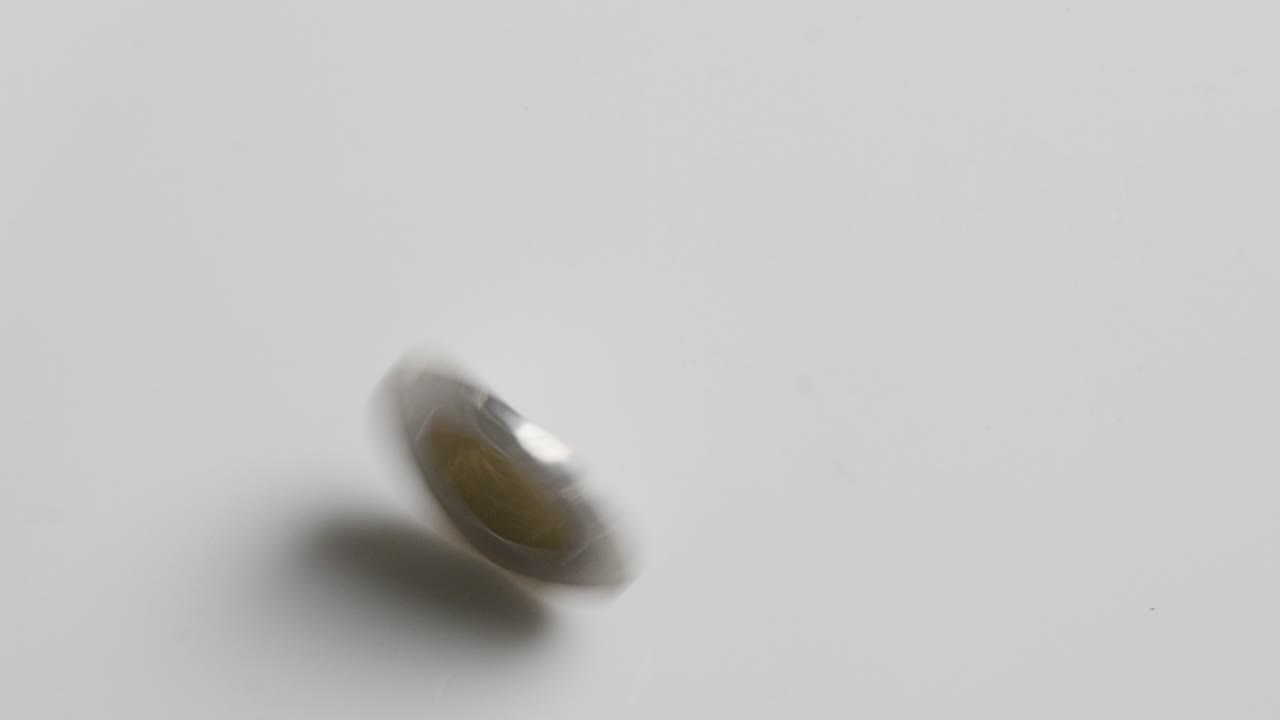 A single silver and gold coin spinning on a white surface before coming to rest. Canadian two dollar coin CAD