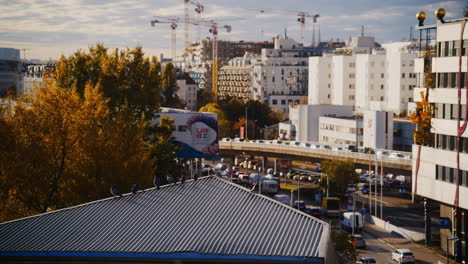 birds sit on top of roof as cars drive by with construction cranes off in distance, spittelau vienna austria