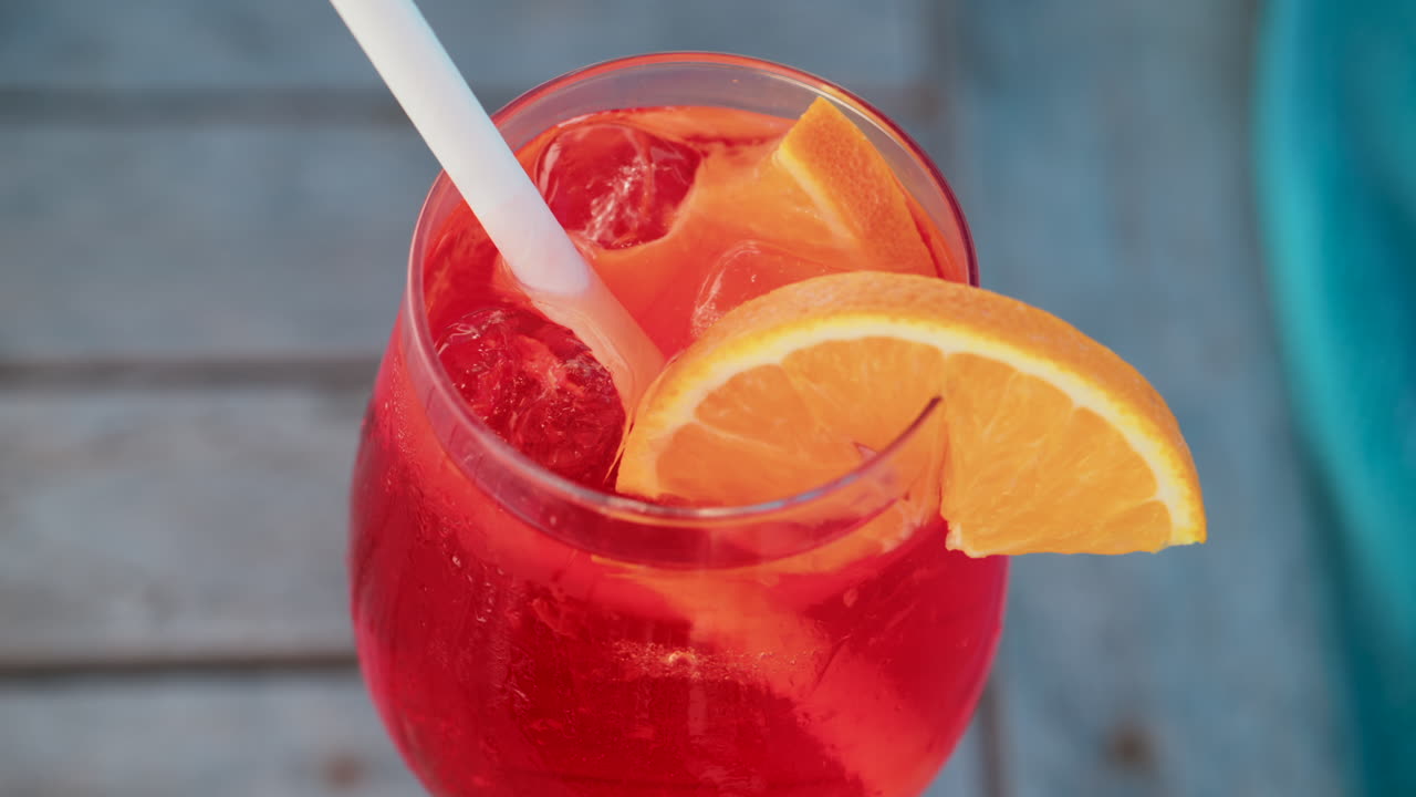 Close up of a refreshing red orange cocktail with orange slice and ice cubes, captured outdoors on a sunny day in Cannes