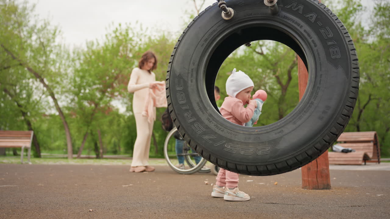 Family Park Scene, Child Near Swing Amidst Greenery, Inclusive Playground With Family And Children Present, Family Enjoying Outdoor Play Area With Trees And Wheelchair Accessibility