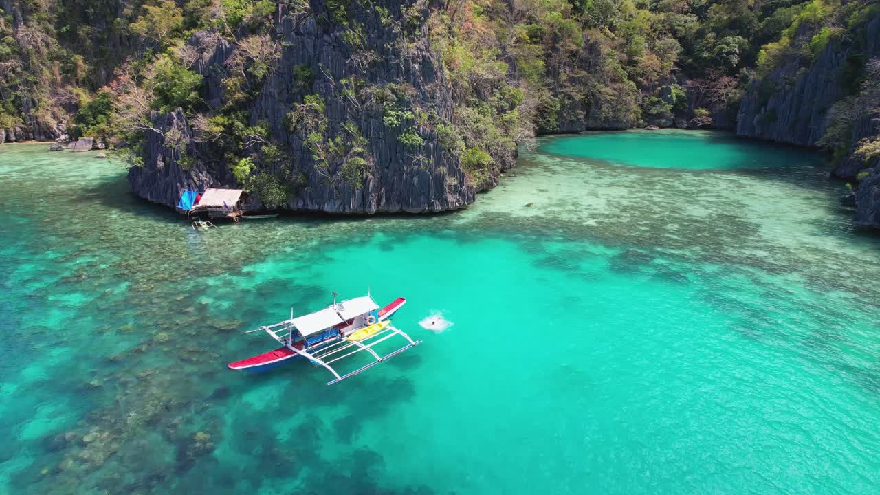 4K drone video of a couple jumping off a boat at Green Lagoon while on a private boat trip from coron in Palawan, Philippines