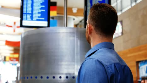 man using mobile while looking at flight information display system