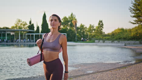 mujer deportista madura pisando la orilla del lago de sol de primer plano. mujer mirando a la cámara