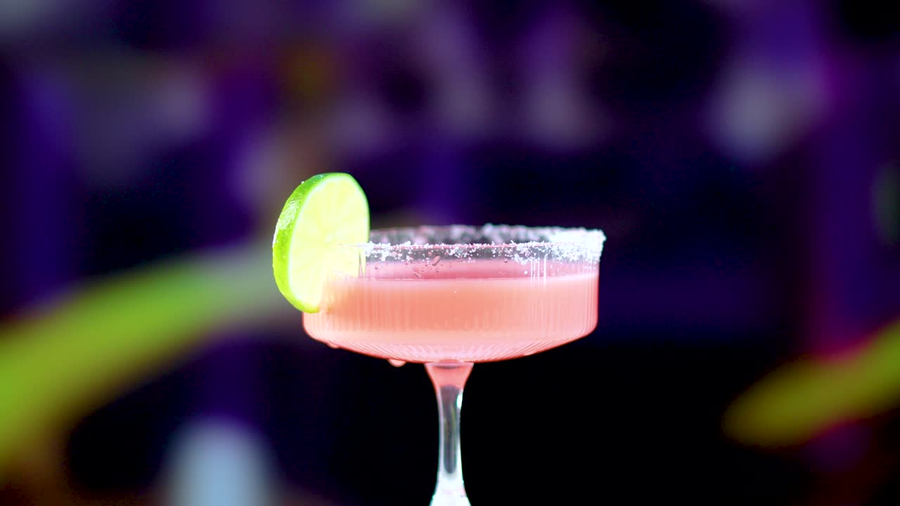 A pink margarita cocktail with a lime slice in a glass, set against a colorful, blurred background