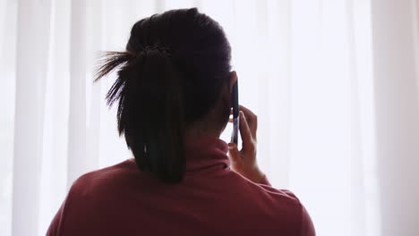 Asiatische-Frau,-Die-Am-Fenster-Mit-Sonnenlicht-Telefoniert