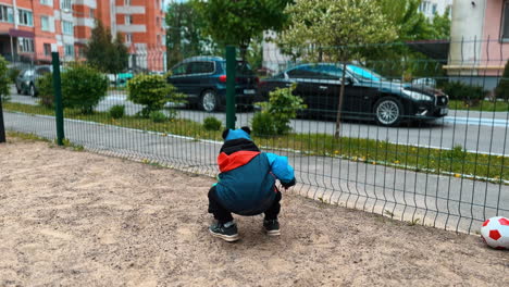 little kid picks up some sand from the ground and throws it away through the fence. toddler has active time outdoors.