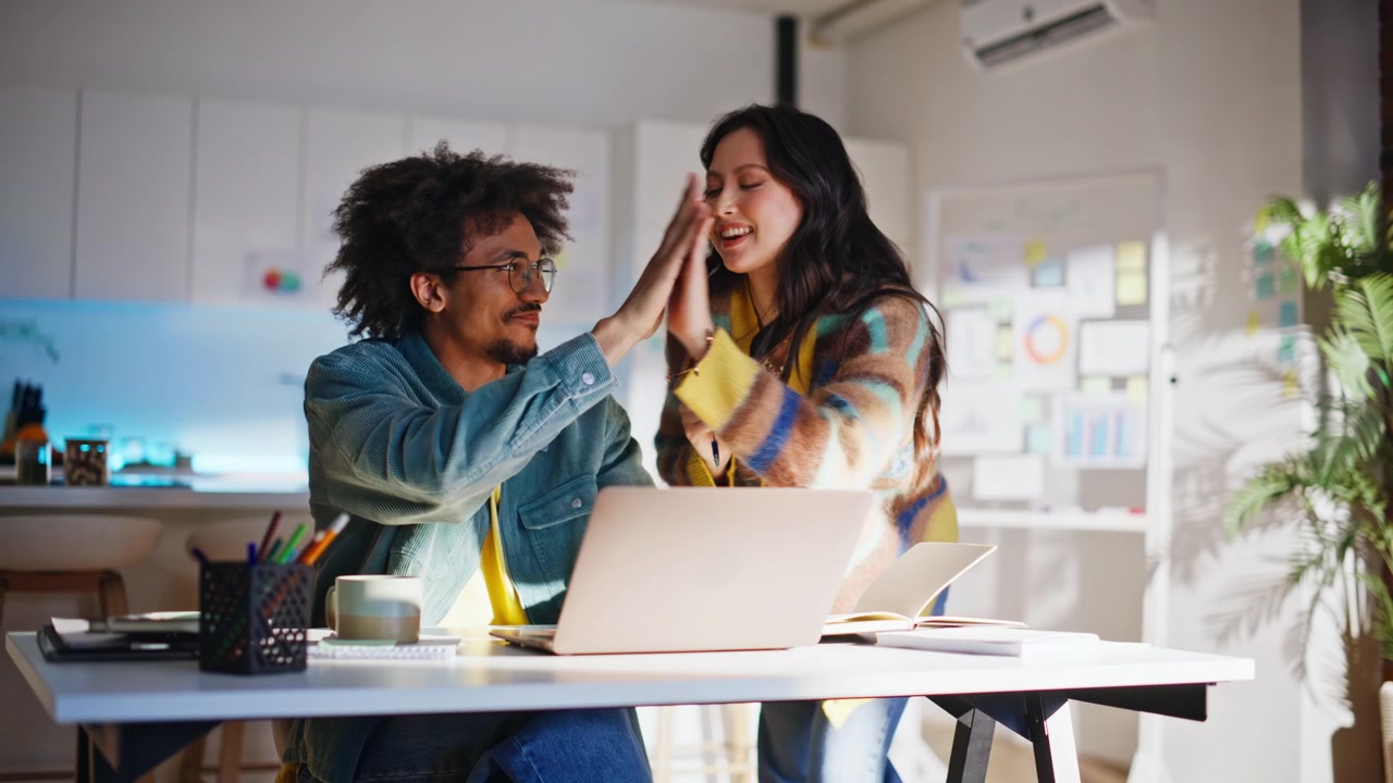 Startup partners discussing project laptop. Coworkers high five celebrating.