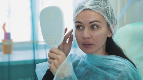 woman with cap on head looks into oval mirror in clinic