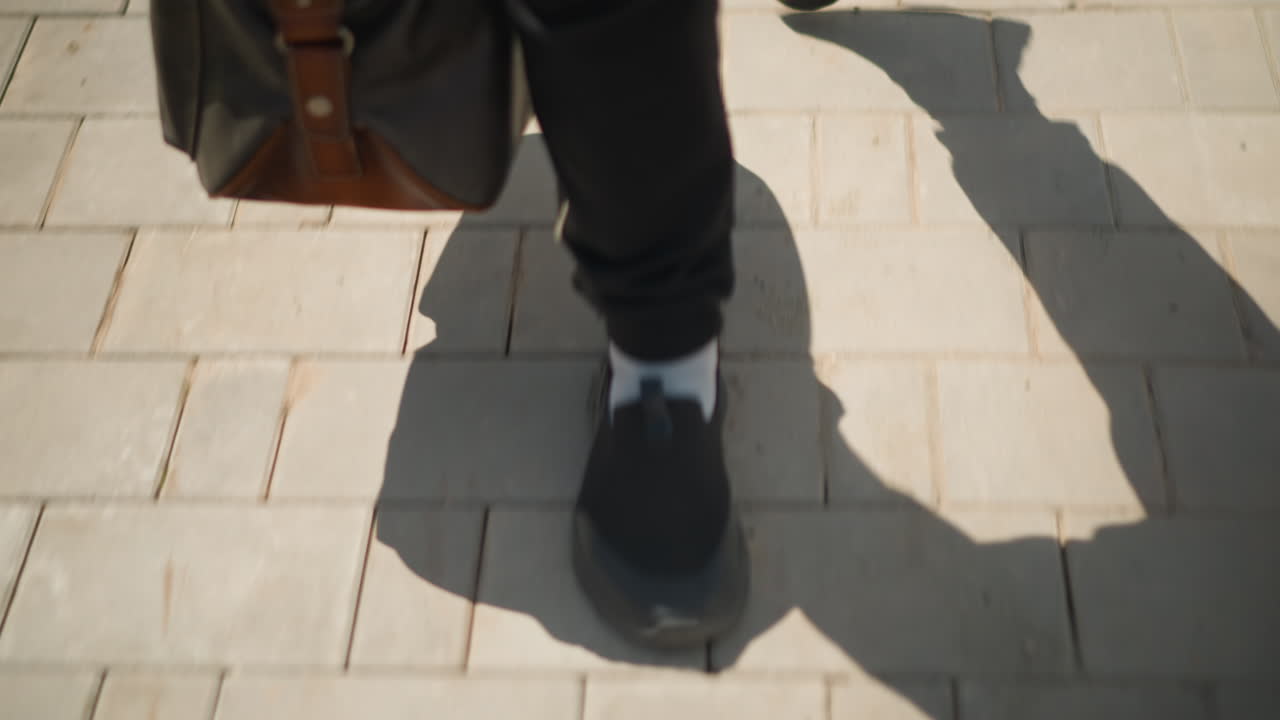 Unas zapatillas avanzan sobre el pavimento iluminado por el sol, primer plano de unas zapatillas deportivas caminando por un sendero urbano iluminado, toma detallada que captura el movimiento de las zapatillas en una calle de la ciudad bañada por el sol con baldosas texturizadas.