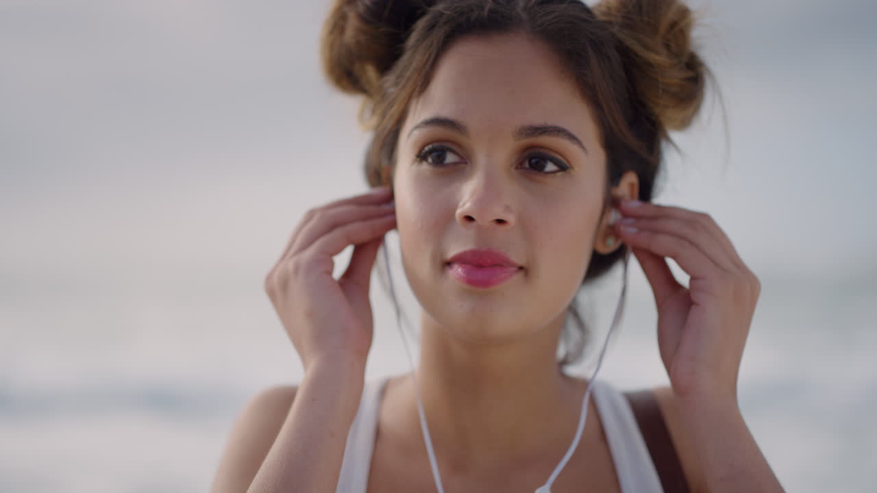 ritratto ravvicinato di una giovane donna felice che indossa gli auricolari sorridendo e ascoltando musica sulla spiaggia sul mare