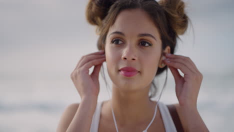 Primer-Plano-Retrato-De-Una-Joven-Feliz-Se-Pone-Auriculares-Sonriendo-Disfrutando-Escuchando-Música-En-La-Playa-Junto-Al-Mar