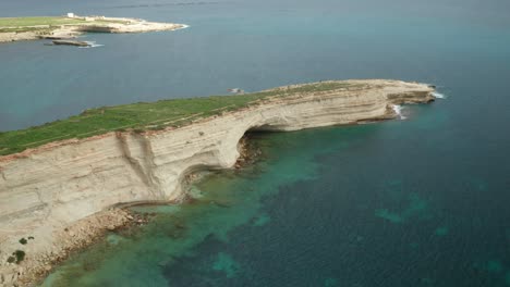 aerial: ras il-fniek point in marsaxlokk with majestic turquoise mediterranean sea waves crashing in shore