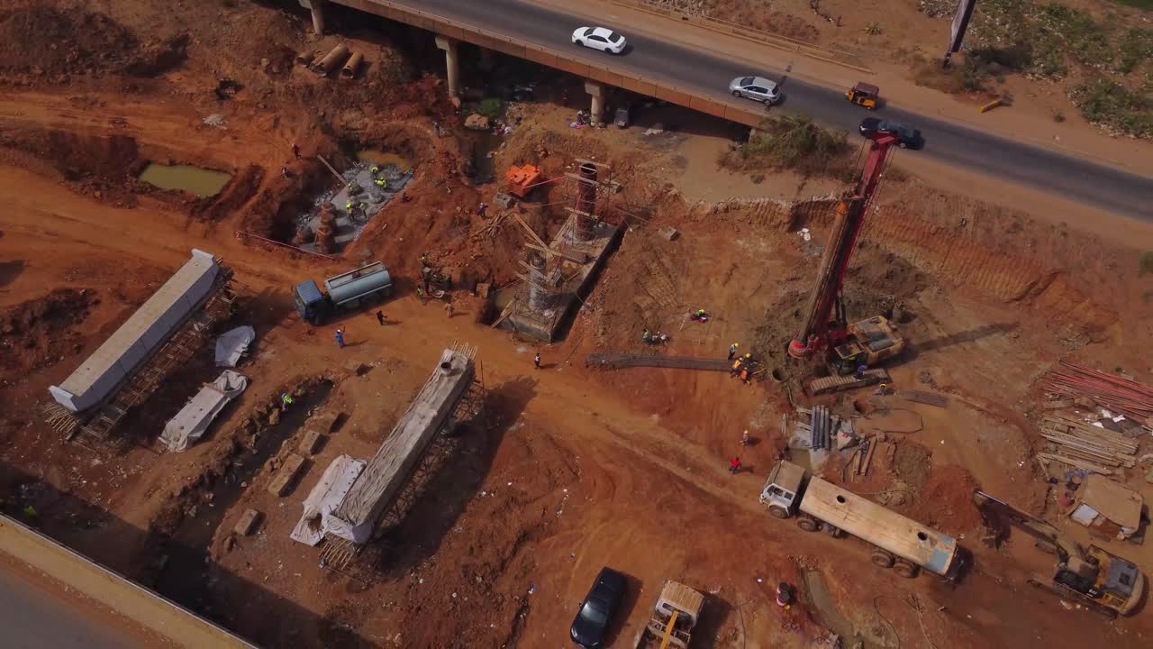 Bela vista aérea de pilares sendo construídos como parte de uma grande rodovia em Abuja, Nigéria. Construção de ponte em um dia ensolarado em Abuja; trabalhadores da obra estão trabalhando perto da estrada movimentada.
