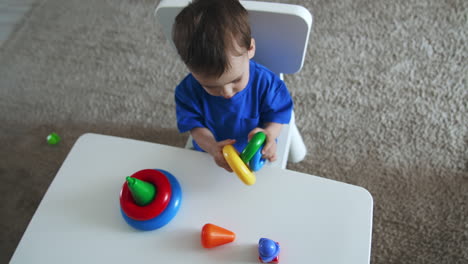 cute smiling baby boy holds the rings in his hands. caucasian child assembling the pyramid. top view.