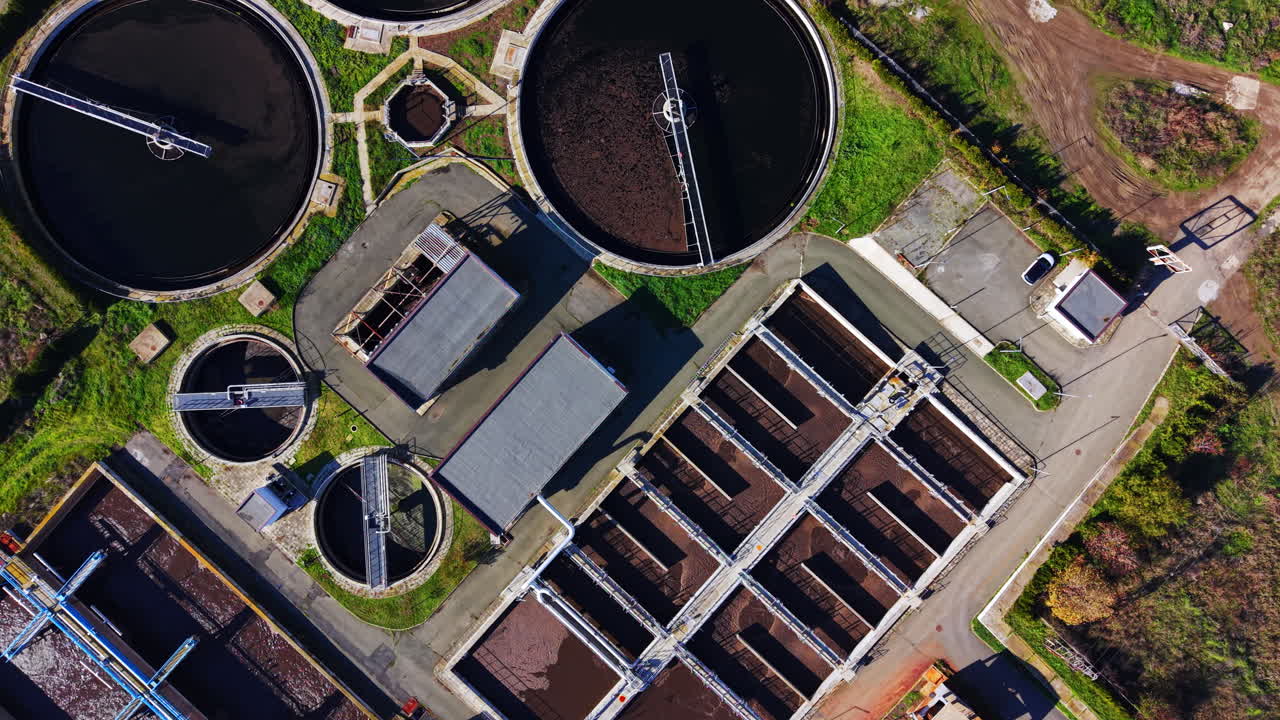 Direct overhead aerial shot of large circular and rectangular filtration tanks at an industrial water treatment facility with green grass