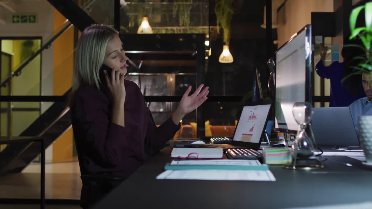 Video af kaukasisk forretningskvinde, der taler i smartphone og bruger computer om natten på kontor.