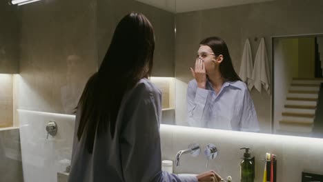 woman applying face mask and facial roller in bathroom