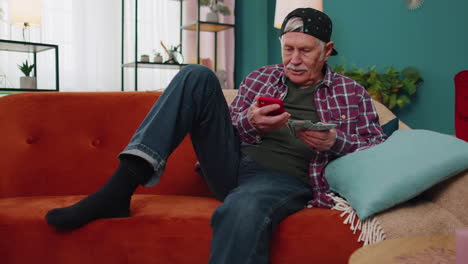 smiling senior man holding money cash and smartphone, satisfied of income, planning family budget