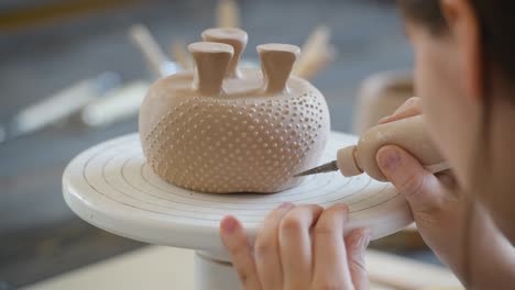 primer plano de la parte inferior de la taza, que está siendo decorada en un estudio de cerámica. manos profesionales femeninas haciendo puntos de arcilla o gotas en la superficie del jarrón con una herramienta especial de exprimir