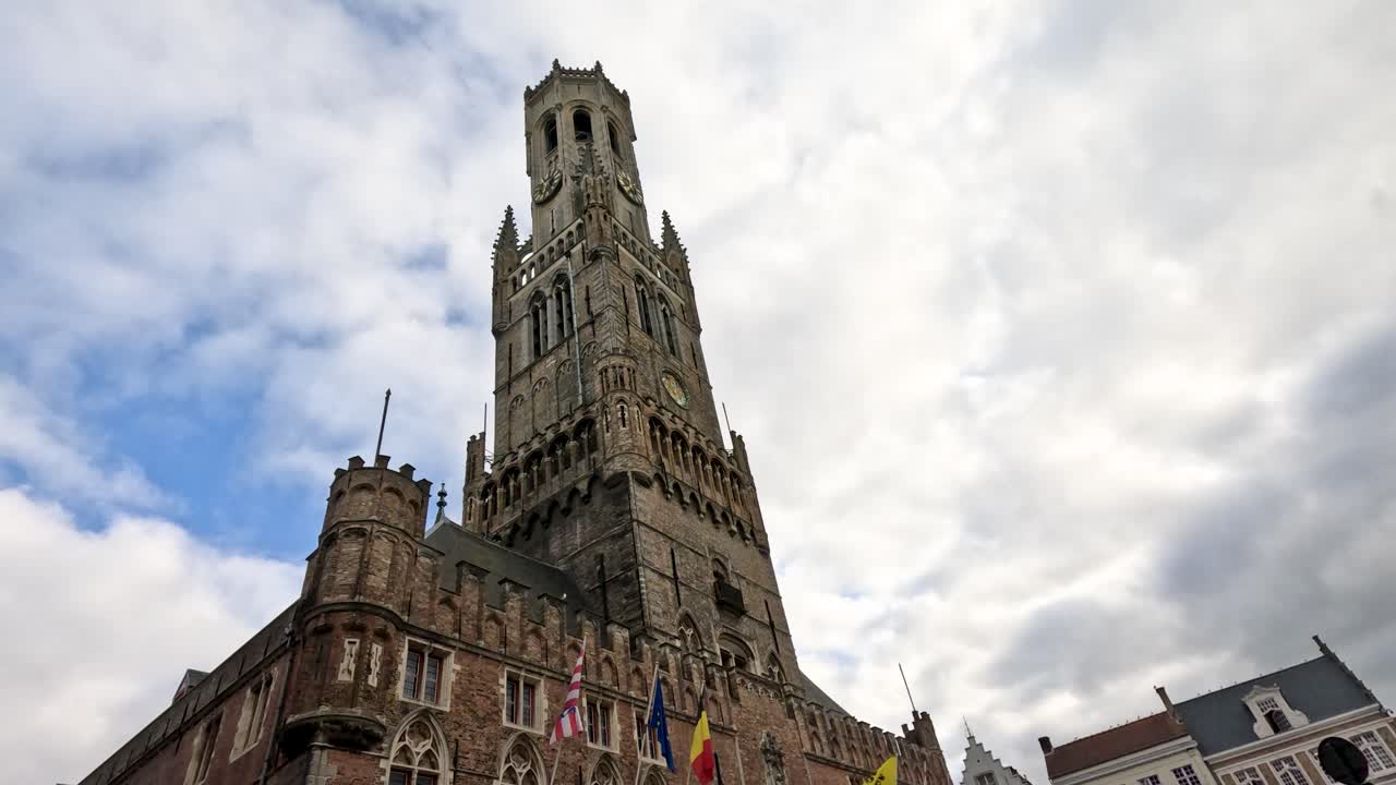 Camera tilts upward past Bruges’ historic Belfry tower, showcasing Gothic architecture and city square
